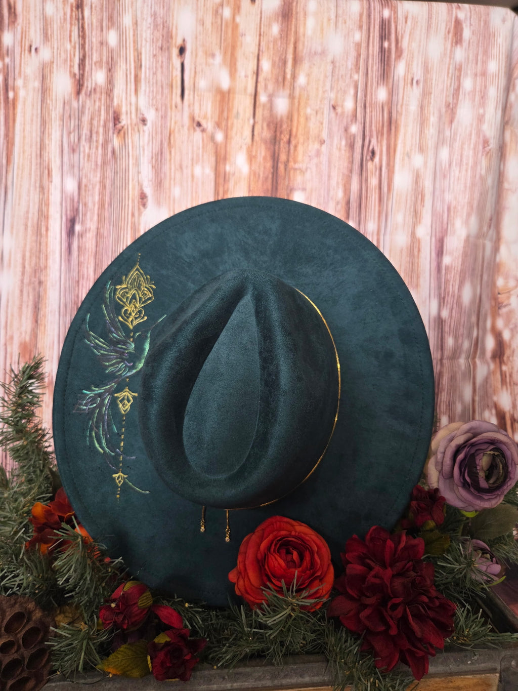 Green velvet hat with embroidery on a wooden surface with flowers and pine cones.