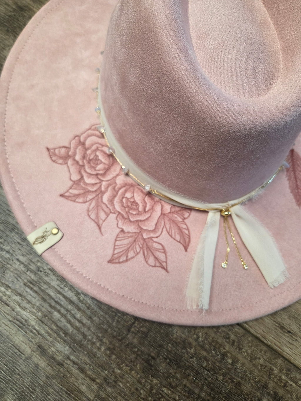 Pink hat with floral embroidery and a white ribbon on a wooden surface