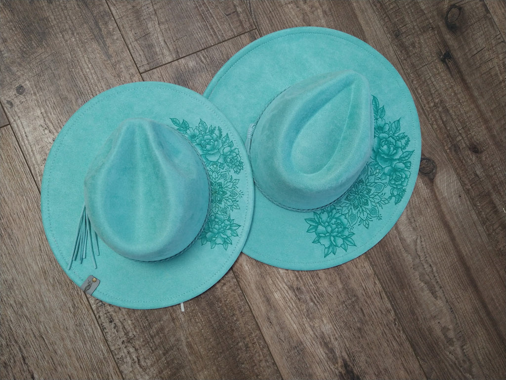 Two turquoise hats with floral designs on a wooden surface