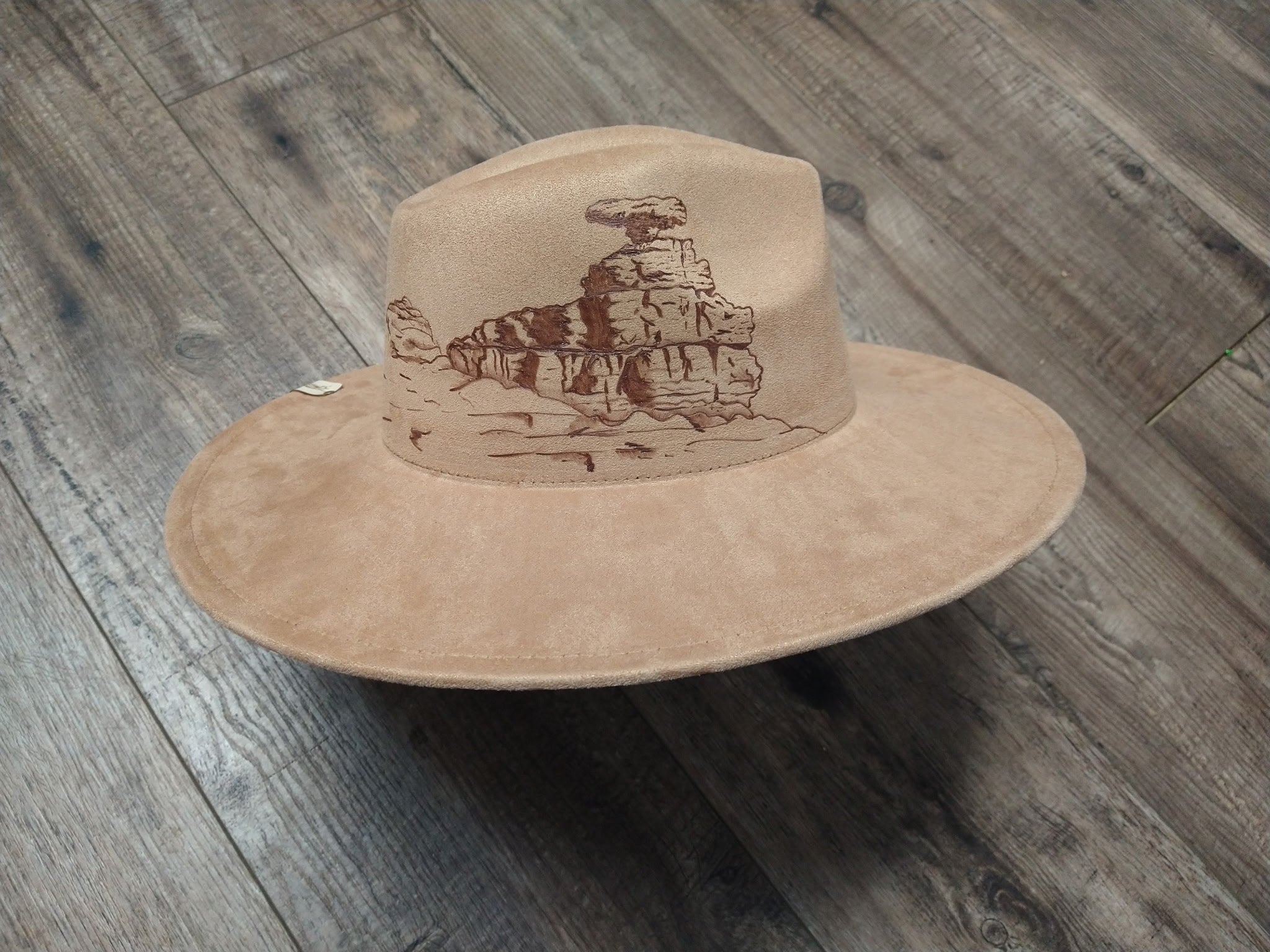 Beige cowboy hat with a desert landscape design on a wooden surface