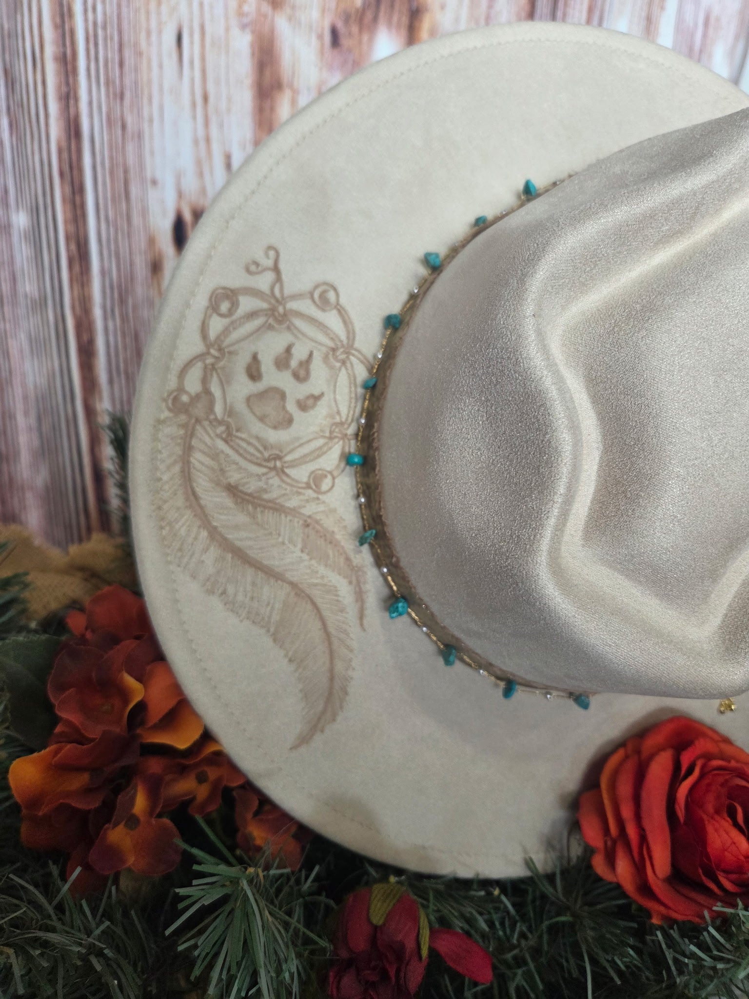 White cowboy hat with decorative band and paw print design, surrounded by flowers and greenery.
