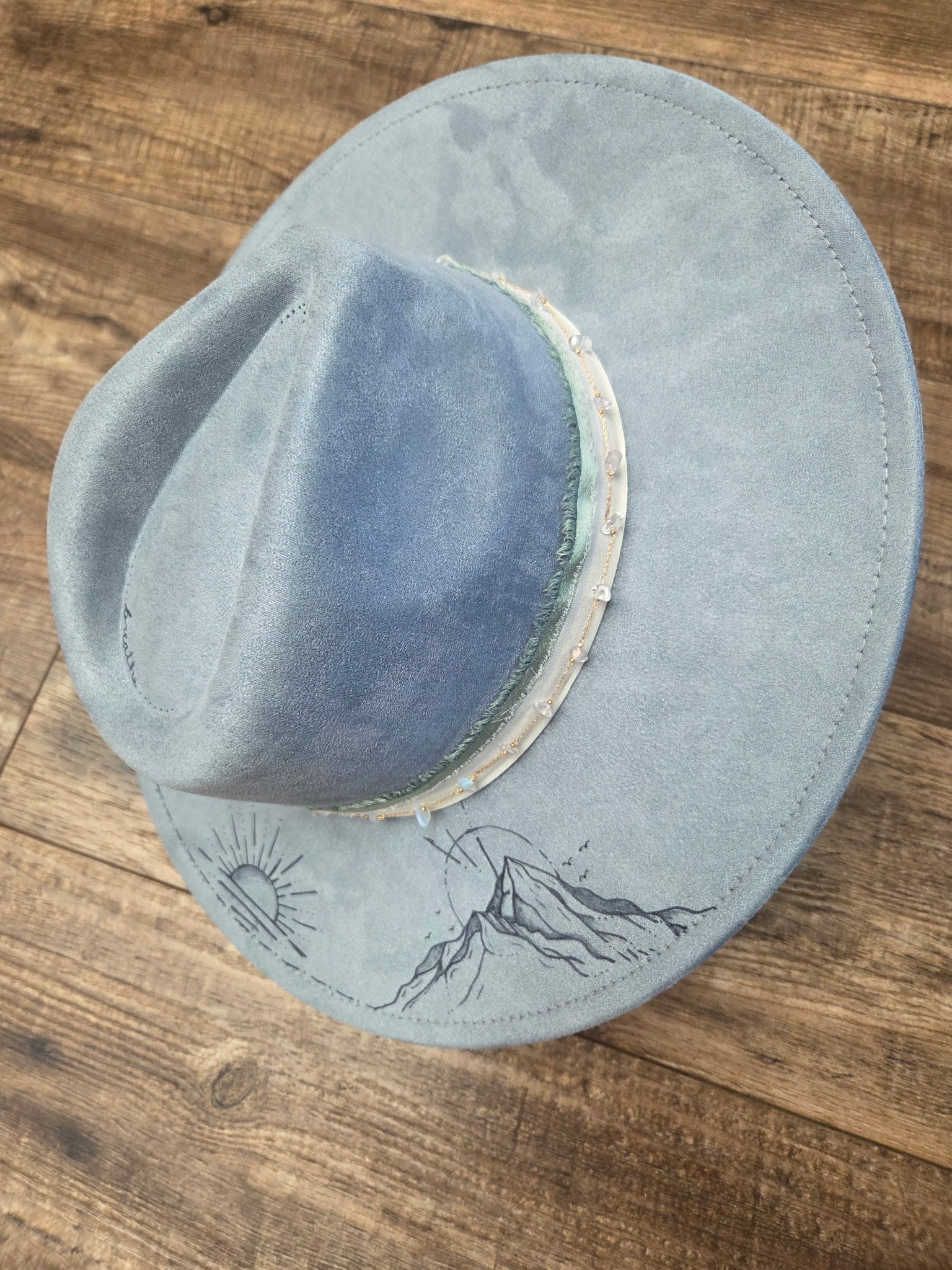 Blue suede hat with mountain design on a wooden surface