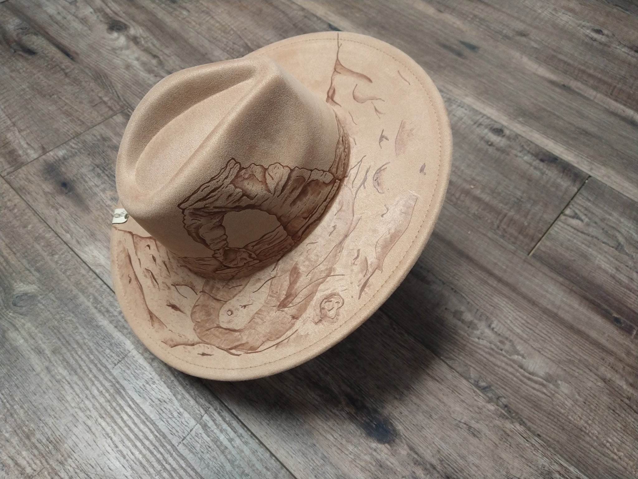 Beige cowboy hat with engraved design on a wooden floor