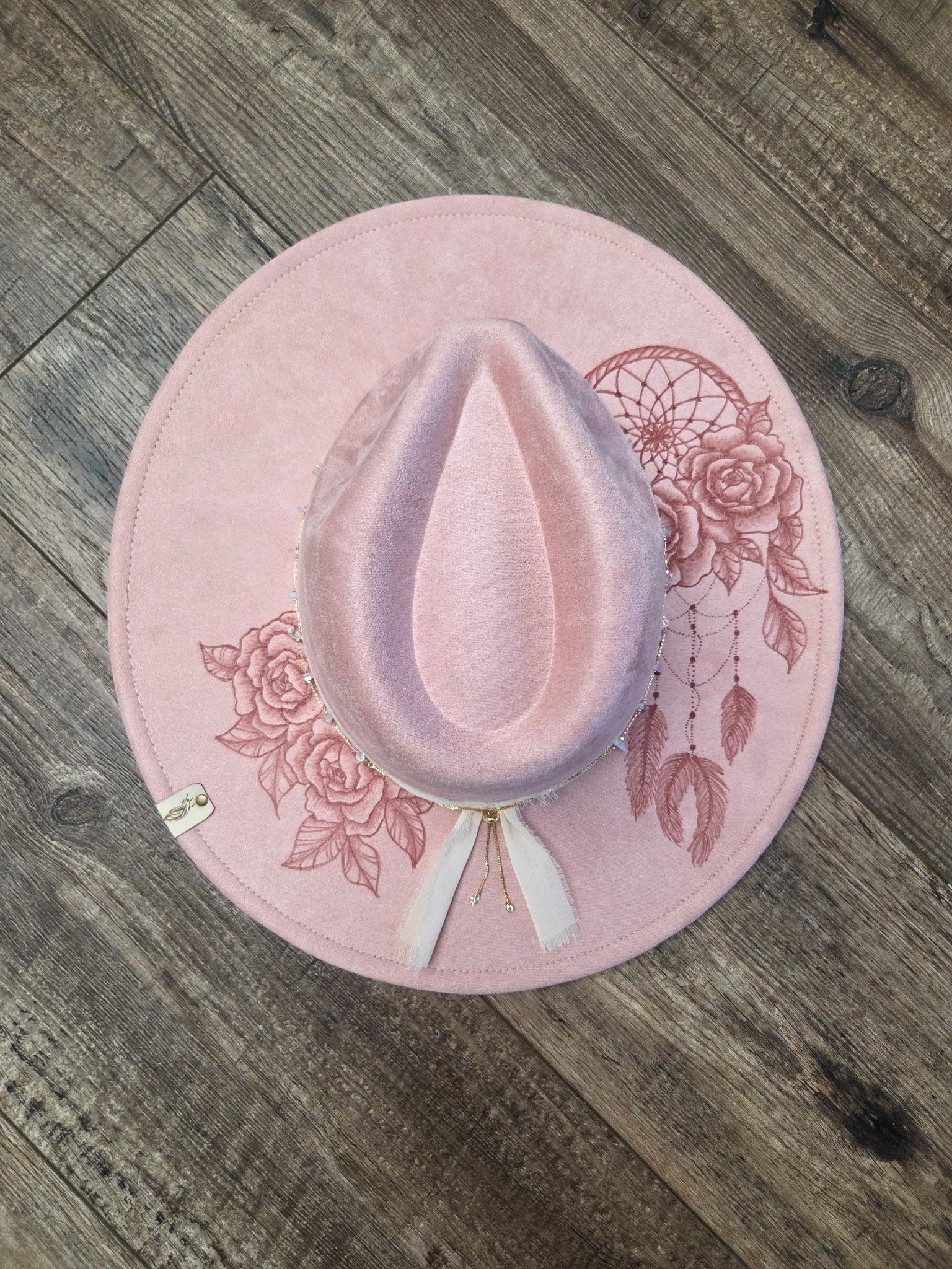 Pink hat with floral and dreamcatcher designs on a wooden surface