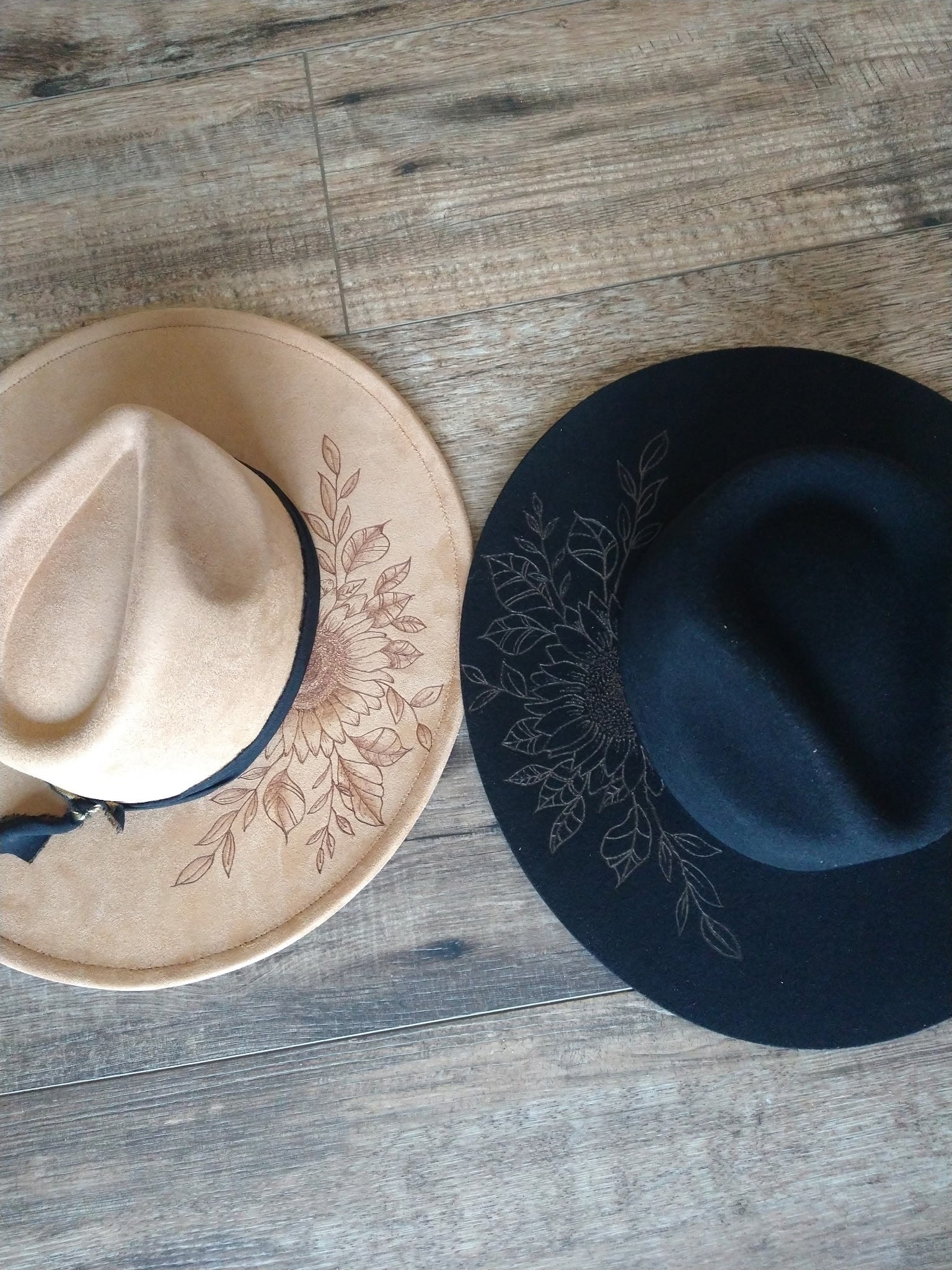 Two hats, one beige and one black, with floral embroidery on a wooden surface.